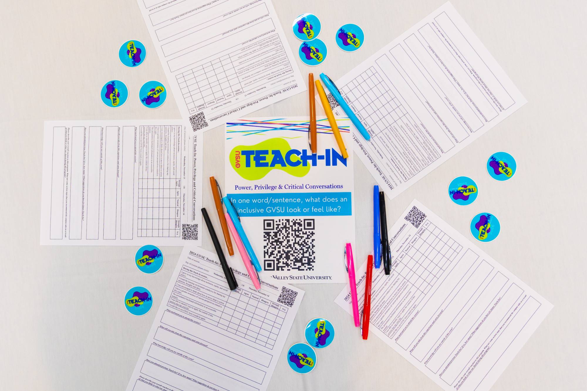 White table with teach-in survey flyer on it, with Teach-In stickers and pens and markers surrounding them